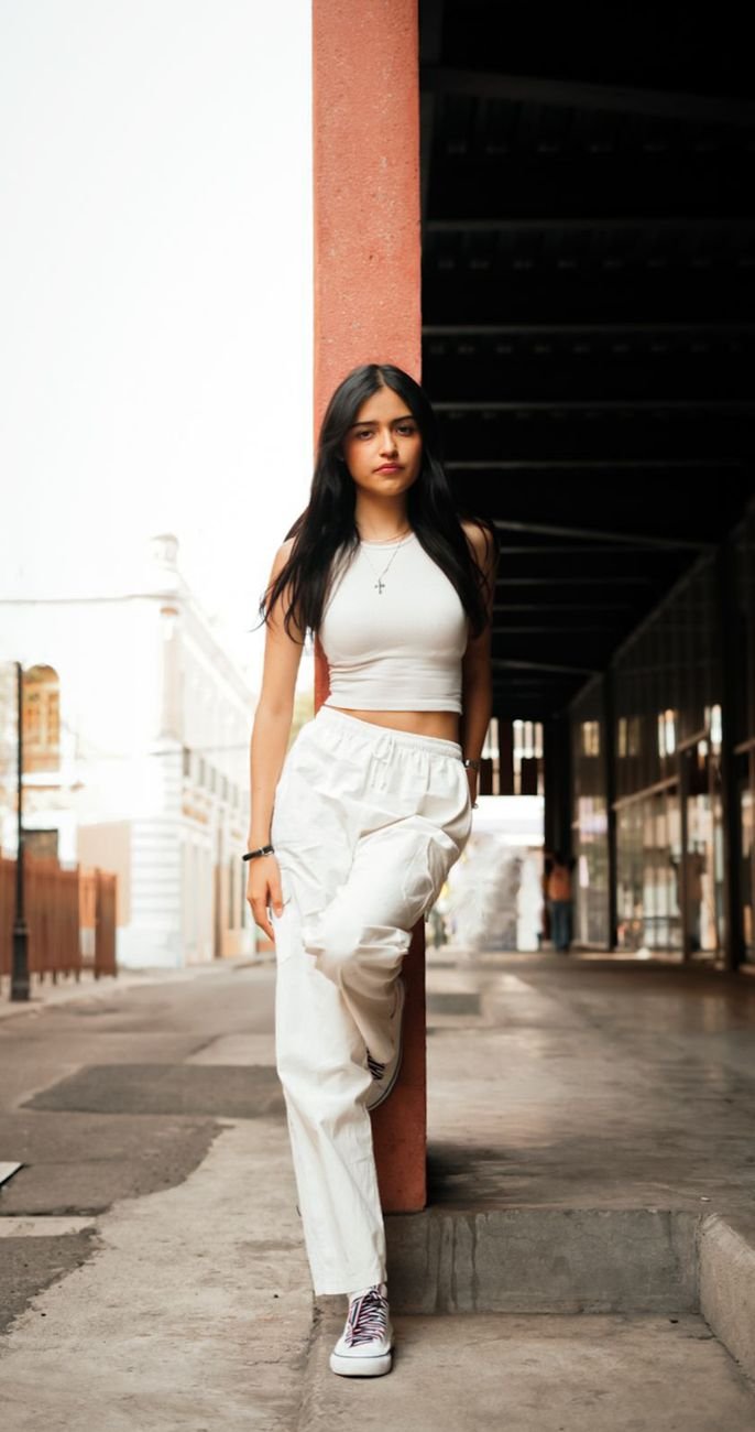 Stylish woman posing in urban setting, wearing trendy white outfit with confident look.