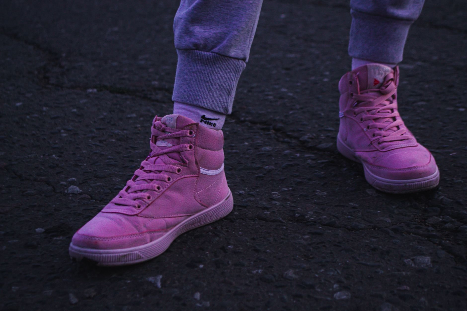 Close-up of pink sneakers on a dark urban street, showcasing street style fashion.